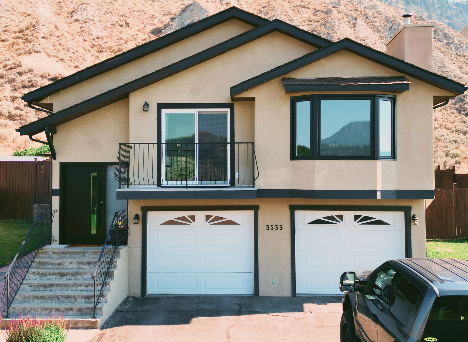 Tan stucco BC home with new black-framed windows and balcony door